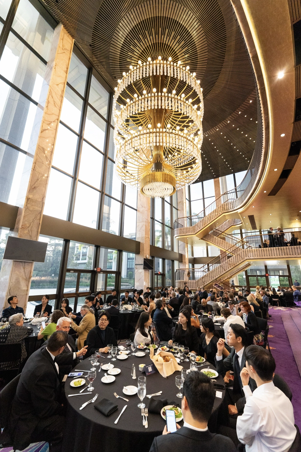 Designers dining beneath a large golden chandelier beside a sweeping staircase